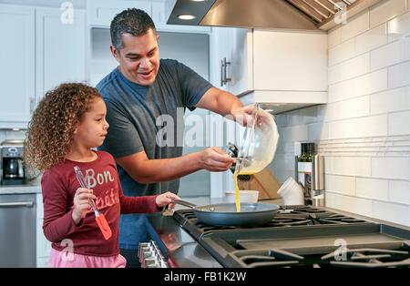 Padre aiutando la figlia cuocere la frittata sul piano di cottura in cucina, versando l'uovo in padella Foto Stock