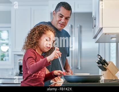 Padre aiutando la figlia cuocere sul piano di cottura in cucina Foto Stock