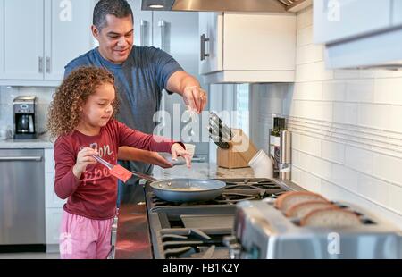 Padre aiutando la figlia cuocere sul piano di cottura in cucina, spargendo il formaggio Foto Stock