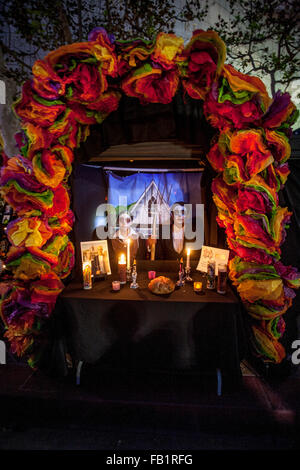 Indossando il trucco che assomiglia alla faccia di La Calavera Catrina ('Dapper scheletro') giustapposti con il famoso concedere il legno dipinto 'Gotico americano' un paio di porre a un altare in onore di un parente deceduto durante il giorno dei morti o Dia de Muertos holiday amo Foto Stock