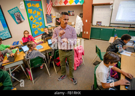 Un ispanico quinta elementare insegnante guarda il suo multirazziale gli studenti lavorano con il computer portatile in una San Clemente, CA, scuola elementare in classe. Foto Stock