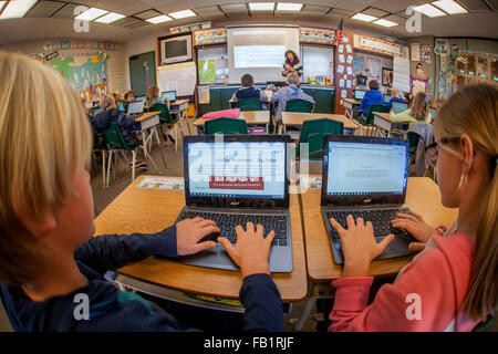 Terzo grado agli studenti di inserire informazioni nel loro Google Chromebook computer laptop in una San Clemente, CA, scuola elementare in classe. Nota concentrazione, insegnante e proiettata immagine del computer sullo schermo in background. Foto Stock