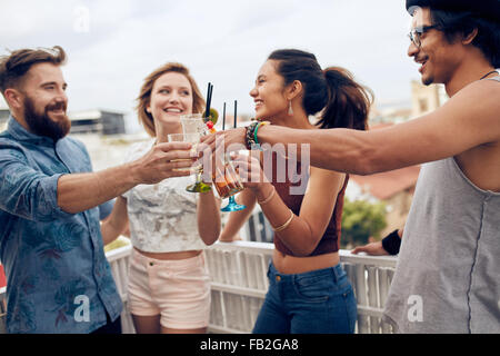 Gli amici sorseggiando un cocktail a una festa. Amici divertendosi e bere un cocktail all'aperto sul tetto insieme. Gruppo di ven Foto Stock