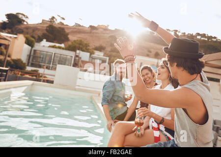 I giovani seduti sul bordo della piscina godendo di una parte. Giovane donna cantare durante una festa. Multirazziale havin amici Foto Stock