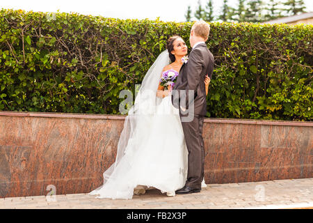 Coppie in viaggio di nozze che abbraccia la sposa tenendo un mazzo di fiori in mano Foto Stock