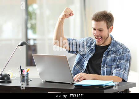 Euforico vincitore uomo felice usando un computer portatile in una scrivania a casa Foto Stock