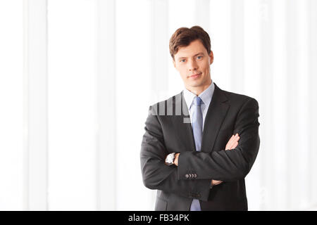 Ritratto di imprenditore bello in piedi vicino a finestre in ufficio Foto Stock