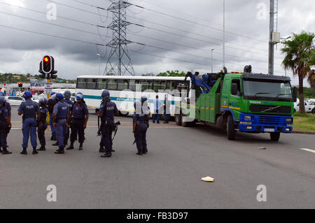 Durban, Sud Africa. 8 gennaio, 2016. La polizia antisommossa stand in corrispondenza di una intersezione mentre un carrello di traino rimuove un Durban busto comunale che è stato abbandonato da colpisce i conducenti di autobus in corrispondenza di una intersezione sulla autostrada Mangosuthu a Durban è la seconda più grande borgata di Umlazi. Il personale del servizio di autobus non sono state versate loro slaries o bonus per il mese di dicembre, mentre alcune sono anche rivendicazione che Tansnat CC, la società che gestisce il servizio per il comune, non ha pagato il loro fondo di previdenza. Credito: Giordano Stolley/Alamy Live News Foto Stock