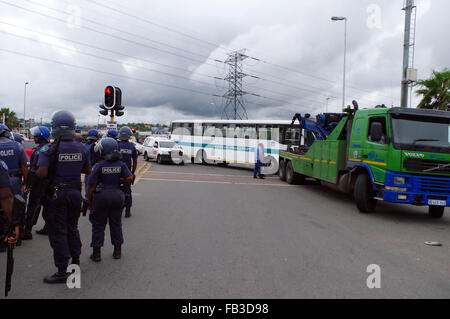 Durban, Sud Africa. 8 gennaio, 2016. La polizia antisommossa stand in corrispondenza di una intersezione mentre un carrello di traino rimuove un Durban busto comunale che è stato abbandonato da colpisce i conducenti di autobus in corrispondenza di una intersezione sulla autostrada Mangosuthu a Durban è la seconda più grande borgata di Umlazi. Il personale del servizio di autobus non sono state versate loro slaries o bonus per il mese di dicembre, mentre alcune sono anche rivendicazione che Tansnat CC, la società che gestisce il servizio per il comune, non ha pagato il loro fondo di previdenza. Credito: Giordano Stolley/Alamy Live News Foto Stock