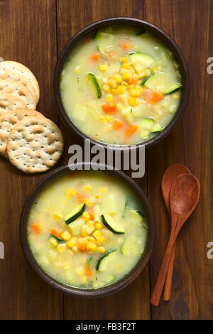 Mais vegetariani e la zucchina chowder servita in due ciotole rustico, saltine cracker e cucchiai di legno sul lato Foto Stock