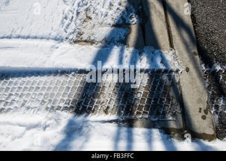 Battistrada del pneumatico nella neve sul marciapiede che conduce alla strada Foto Stock