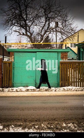 Donna vestita di nero fur passeggiate passato un verde porta di garage Foto Stock