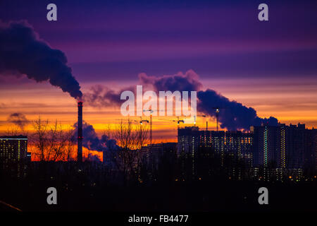 Città moderna di sera al tramonto. Esce del fumo le tubazioni degli impianti e fabbriche del moderno quartiere su t Foto Stock