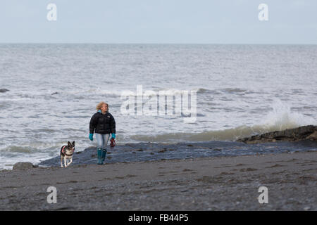 Donna che cammina il suo cane lungo la spiaggia in inverno Foto Stock