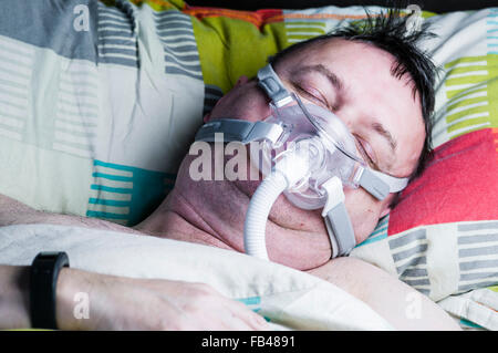 Una di mezza età, sovrappeso uomo che indossa una maschera CPAP mentre dorme nel letto Foto Stock