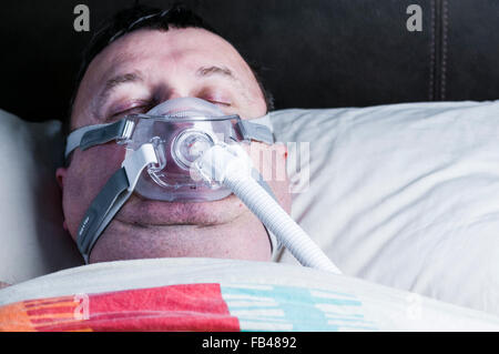 Una di mezza età, sovrappeso uomo che indossa una maschera CPAP mentre dorme nel letto Foto Stock