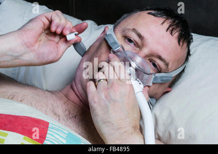 Una di mezza età, sovrappeso uomo regola una maschera CPAP prima di andare a dormire Foto Stock