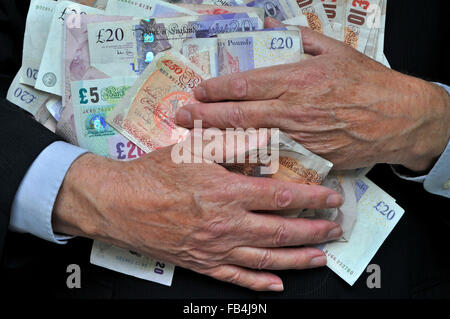 Uomo d'affari in completo di mani più anziane che afferra un mucchio di banconote in sterline, concetto di ricompense avidità, incentivi bonus in denaro non spenderli al Regno Unito Foto Stock