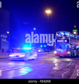 La Metropolitan Police auto con luce blu lampeggiante luce che illuminano il cielo di notte sul Westminster Bridge con bus londinese in attesa al semaforo rosso England Regno Unito Foto Stock