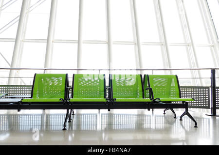 Panca con sedi di verde nella sala partenze dell'aeroporto, con enormi finestre in background. Foto Stock