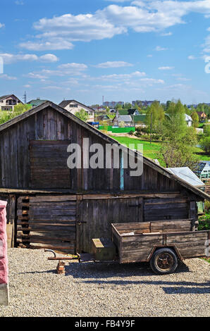 Paesaggio del villaggio. Il vecchio fienile con piccolo rimorchio del trattore. Foto Stock