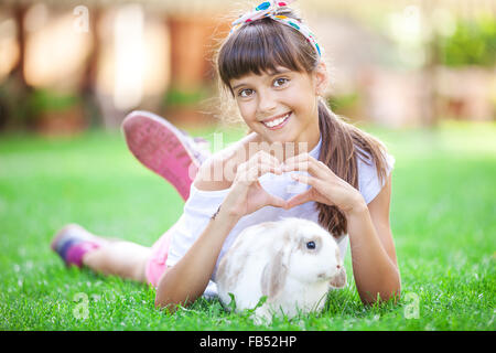 Ragazza sorridente che mostra un segno di cuore con le sue mani su di un coniglio di pet Foto Stock