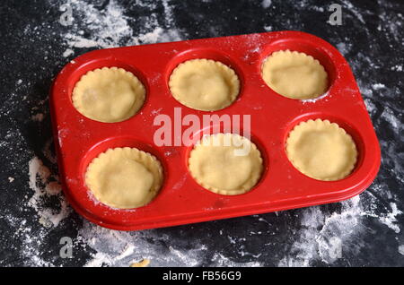 Rosso muffin di silicone vassoio con crudi pasticci di carne macinata al buio su un superficie infarinata Foto Stock