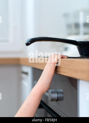 Bambino tocca padella calda sul fornello. Situazione di pericolo a casa. Foto Stock