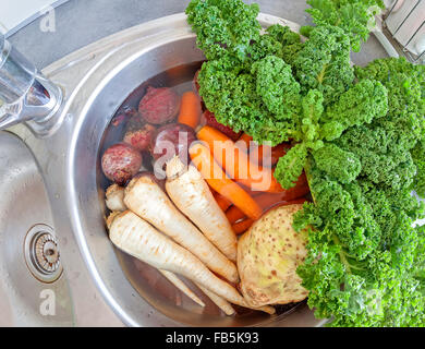 Verdure sporco in un lavello riempito con acqua. Foto Stock