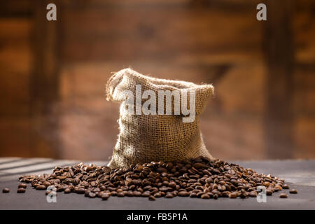 I chicchi di caffè con vapore in borsa sul tavolo nero contro lo sfondo di legno Foto Stock