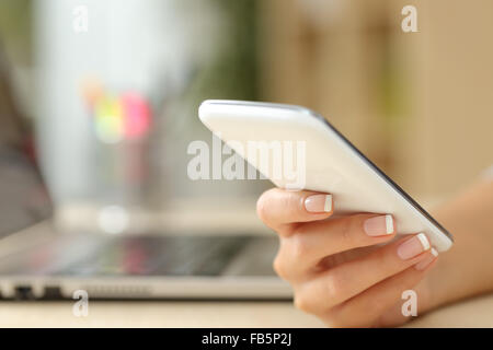 In prossimità di una donna mano utilizzando un bianco smart phone su una scrivania a casa Foto Stock