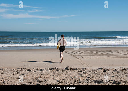 Un uomo che corre in onde con un boogie board presso l'Outer Banks, North Carolina. Foto Stock