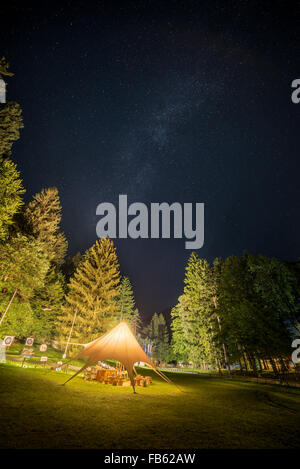 Camping Rifugio si illumina circondato da alberi sotto un cielo notturno pieno di stelle Foto Stock