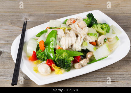 Vista ravvicinata di mescolare bianco fritto di pollo a pezzi con i broccoli, neve, piselli, peperoni e i funghi in piastra bianca. Foto Stock
