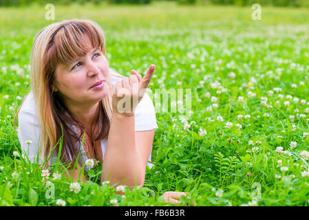 Donna matura su un prato verde che mostra un dito in direzione Foto Stock