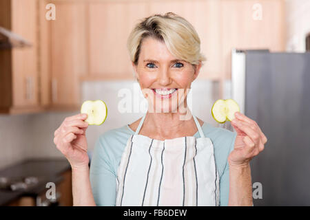 Felice donna senior tenendo le fette di mela in cucina Foto Stock