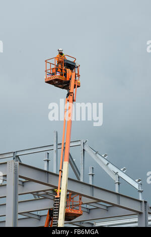 I lavori di costruzione nel Regno Unito : uomini al lavoro in altezza su elevato 'cherry picker' piattaforme, imbullonando insieme il telaio di acciaio di un nuovo sviluppo per il supermercato Tesco e Marks & Spencer store su un sito di costruzione in Aberystwyth, Wales UK Foto Stock