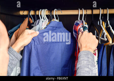 Primo piano di un giovane uomo caucasico scegliendo una camicia da un portabiti Foto Stock