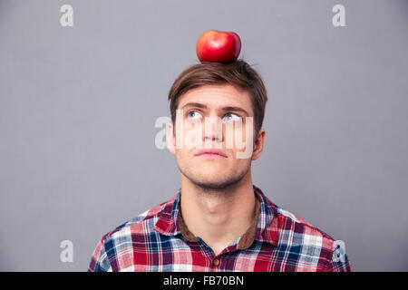 Riflessivo concentrata Giovane Uomo in camicia a scacchi con Apple sulla sua testa su sfondo grigio Foto Stock