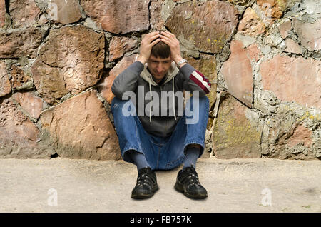 Triste uomo si siede sul marciapiede Foto Stock