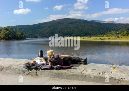Due giovani adulti maschi e femmine motociclisti resto sul lato del fiume Mawddach ammirando le lontane montagne Rhinog. Foto Stock