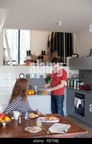 Donna seduta al tavolo da pranzo mentre l uomo prepara la colazione in cucina Foto Stock