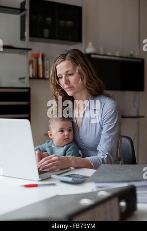 Donna che utilizza computer portatile mentre è seduto con la bambina a casa Foto Stock