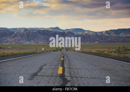 Strada che conduce verso le montagne rocciose contro il cielo nuvoloso Foto Stock
