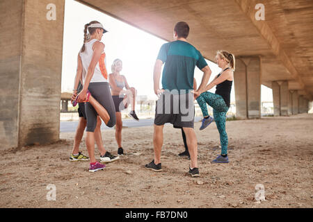 Gruppo di persone sane stretching sotto un ponte della città. Giovani uomini e una donna prendendo una pausa da outdoor training. Foto Stock