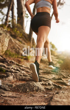 La donna in esecuzione su sentieri rocciosi sul versante della collina. Vista posteriore di immagine femminile la formazione all'esterno. Foto Stock