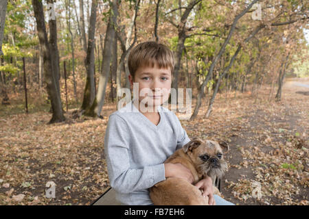 Ritratto di carino ragazzo seduto con il cane nella foresta durante l'autunno Foto Stock