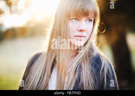 Turbato giovane donna che guarda fuori nella distanza con il sole al suo indietro Foto Stock