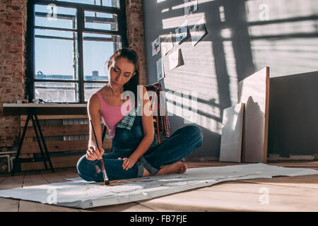 Donna pittura mentre è seduto sul pavimento in art studio Foto Stock