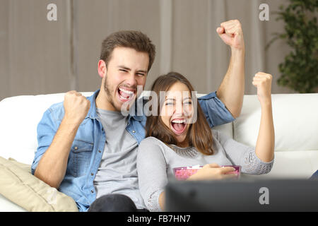 Euforico giovane guardando la TV seduti su un lettino a casa Foto Stock